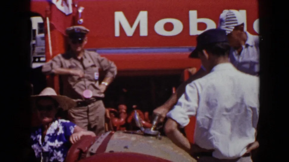 1949 San Diego home-movie frame showing a uniformed man near a red Mobil truck with people gathered around a decorated vehicle.