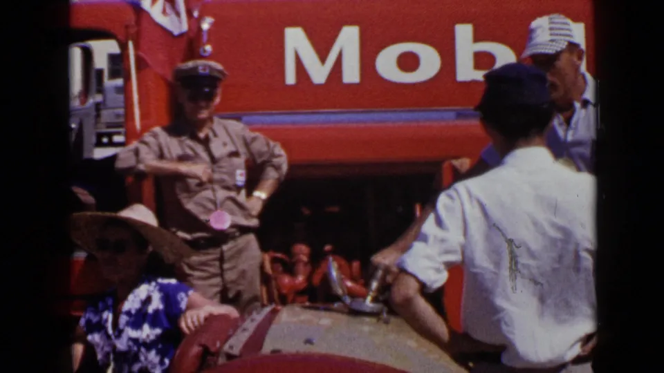 1949 San Diego frame with a red Mobil truck behind spectators and a man in a white shirt standing near a decorated car.