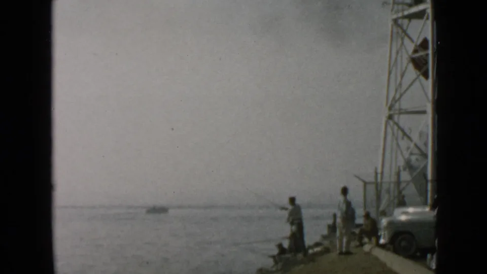 Faded 8mm frame from San Diego showing a small group fishing on a pier with bay water and tower supports in view.