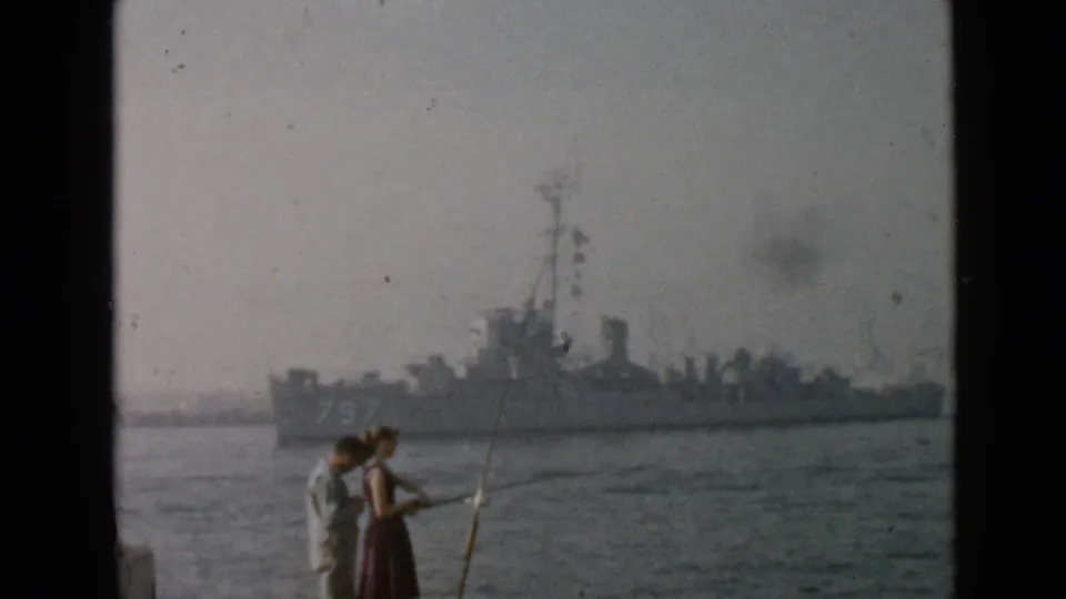 San Diego 1949 home-movie frame showing shoreline fishing in the foreground and a large naval vessel across the harbor.