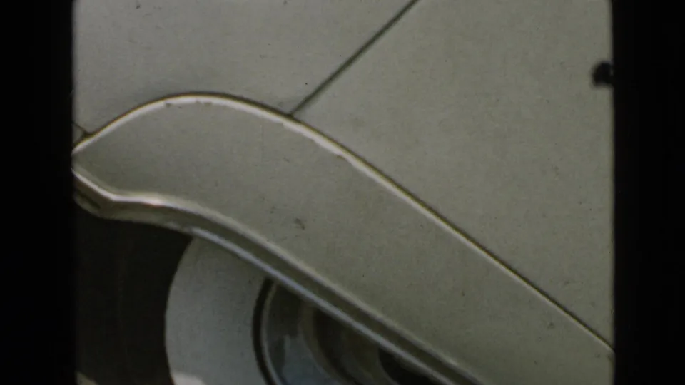 The footage shifts to a close-up of a car body panel with curved chrome trim, seen through soft 8mm color and film wear.