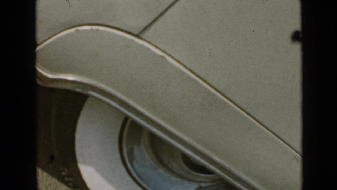 Close view of a pale classic car fender and round headlight on 8mm film.