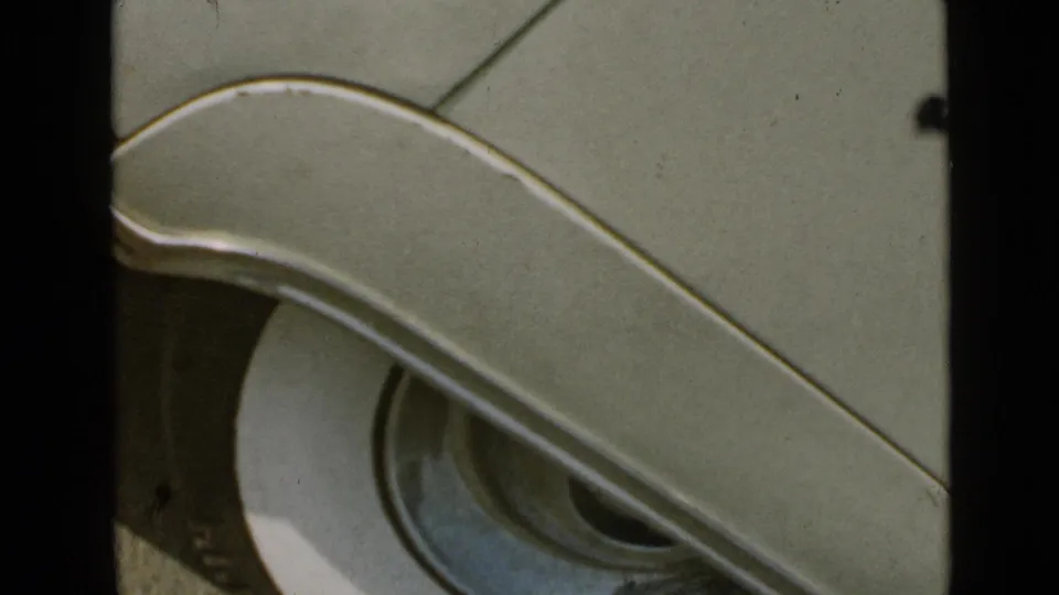 Close-up detail of a pale mid-century car body and headlight, consistent with the supplied 1949 San Diego home-movie clip.