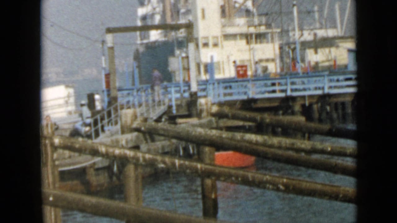 1949 San Diego harbor footage showing a docked cargo ship beyond pier pipes, blue railings, and water in soft 8mm color.