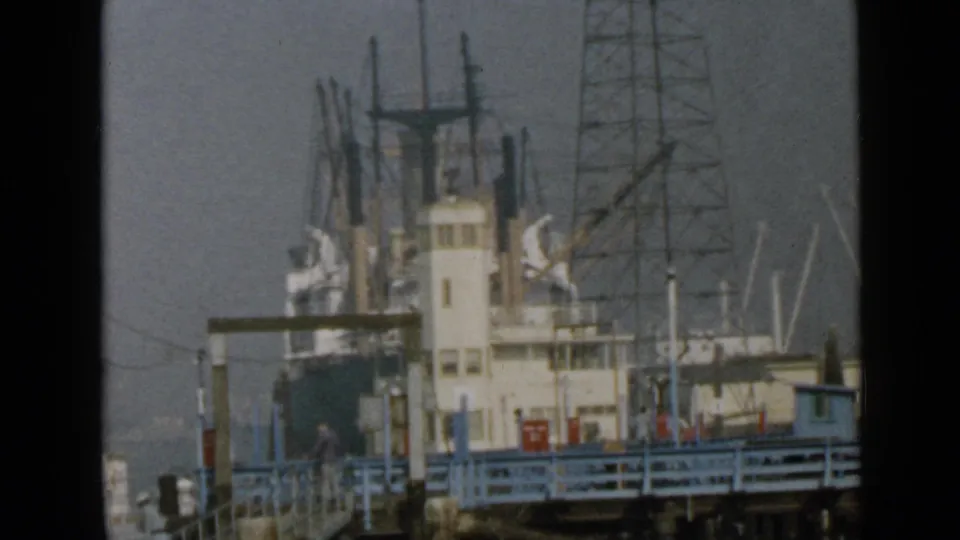 The final frame holds on the San Diego docked ship, with rigging, blue-painted railings, pier structures, and hazy waterfront background.