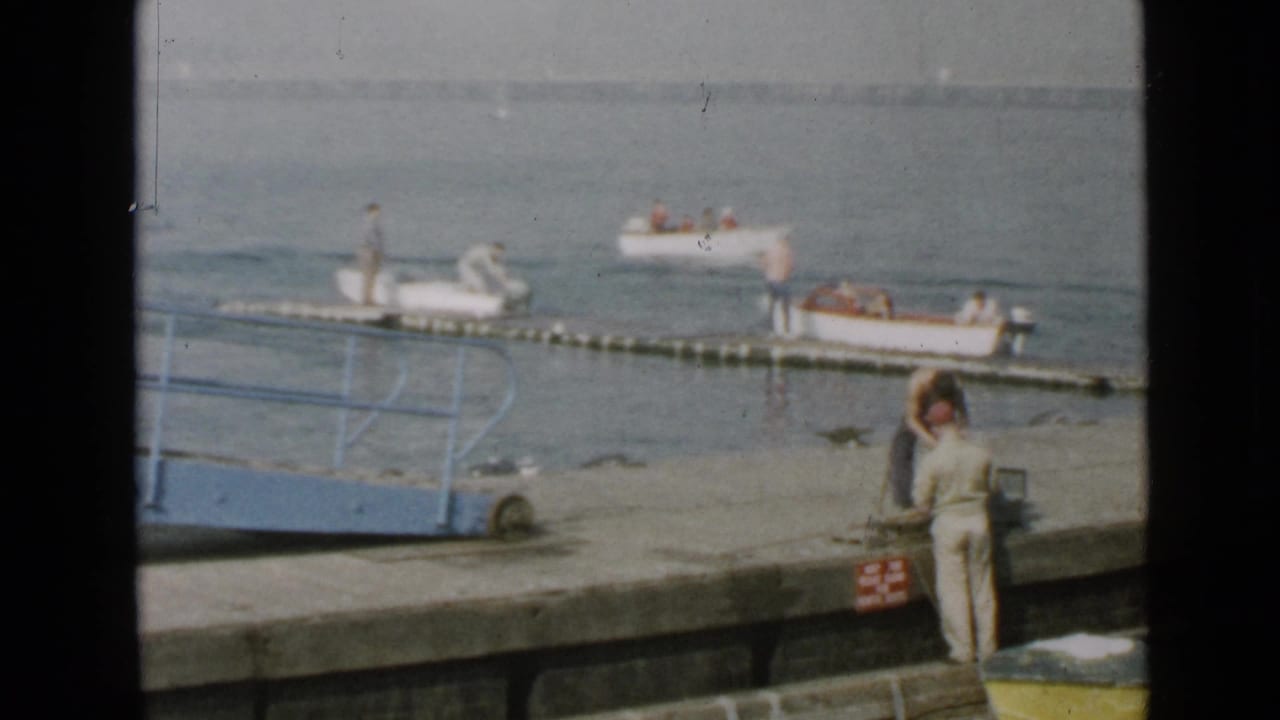 Person on a concrete pier near small boats and a floating dock on calm water.