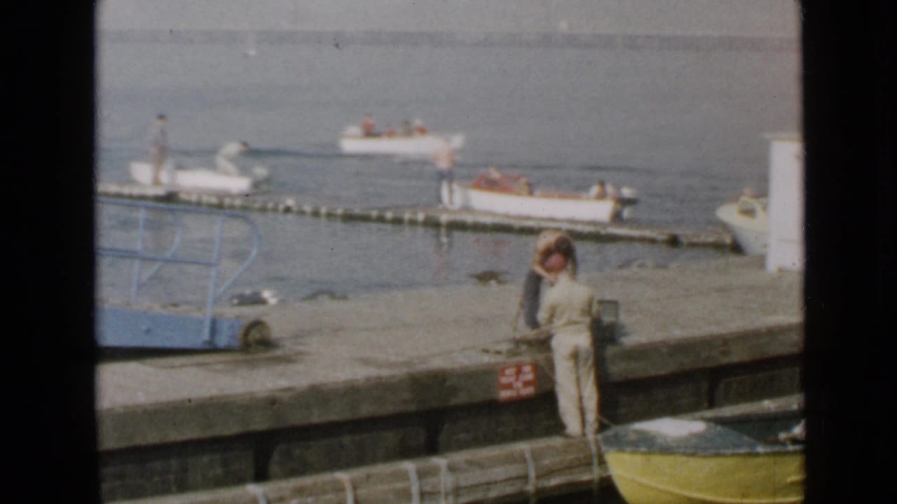 1949 San Diego waterfront frame with a person on the pier and small motorboats near a floating dock.