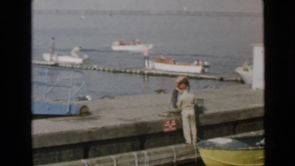 1949 San Diego waterfront frame with a person on the pier and small motorboats near a floating dock.