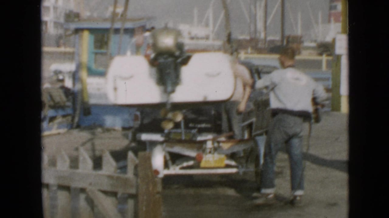 1949 San Diego home-movie frame showing a man beside a small motorboat with an outboard motor near dock equipment.