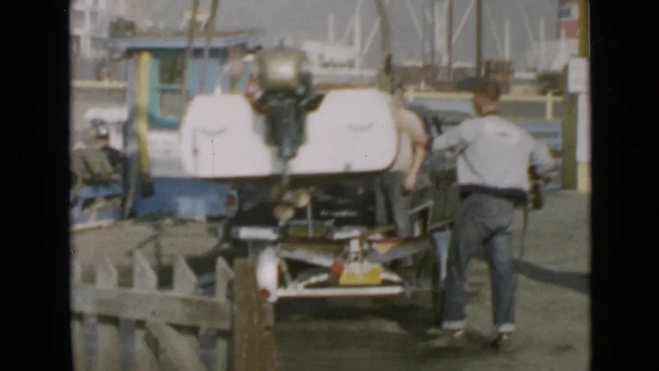 1949 San Diego home-movie frame showing a man beside a small motorboat with an outboard motor near dock equipment.
