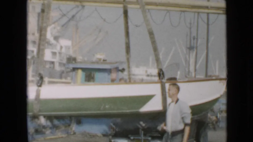 1949 San Diego waterfront frame with a man standing near the hull of a small boat during dockside launch preparation.