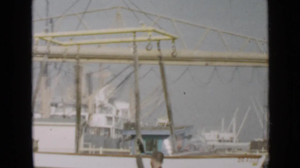 Faded 8mm frame from the San Diego dock area, showing boat rigging, waterfront structures, and a partly visible person near the foreground.