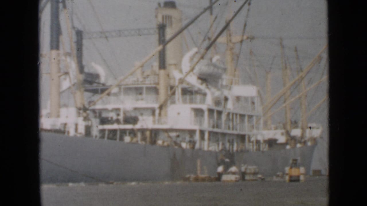 1949 San Diego dockside view of a large cargo ship with cranes, smokestack, workers, and small port equipment near the pier.