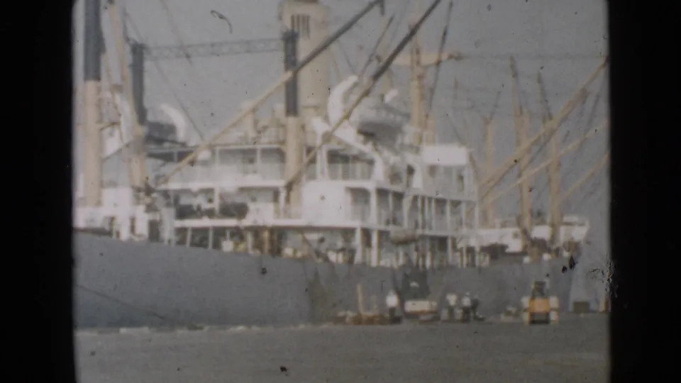 Final 1949 San Diego harbor frame shows the cargo ship, cranes, pier workers, and a yellow dock vehicle in a scratched 8mm home-movie view.