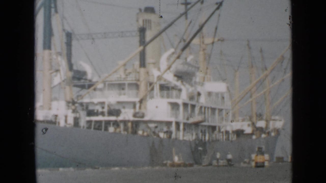 San Diego harbor view of a large cargo ship, crane rigging, and small workboats near the waterline in faded 8mm color.