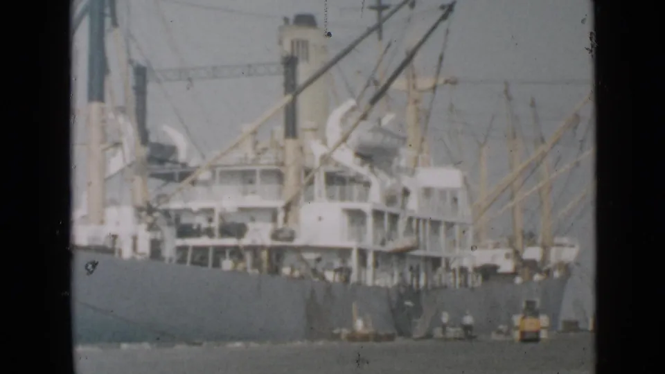 San Diego harbor view of a large cargo ship, crane rigging, and small workboats near the waterline in faded 8mm color.
