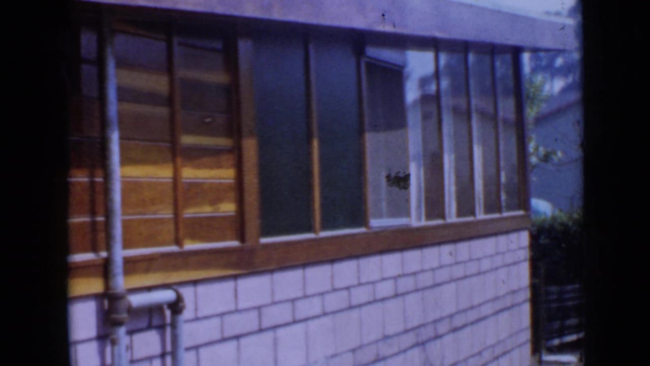 San Diego house exterior in 1949 footage, showing wood-framed windows, pale shingle siding, and exposed pipework.
