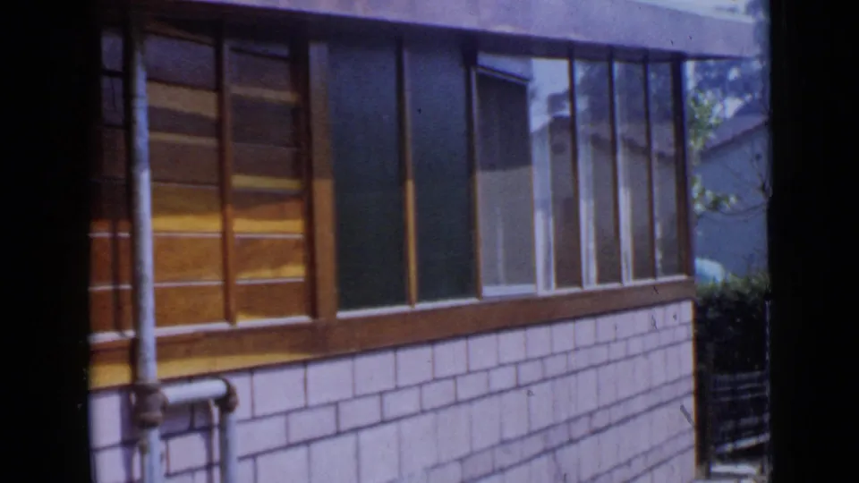 1949 San Diego home exterior view with wood window frames, pale shingle siding, exposed pipes, and a narrow side yard.