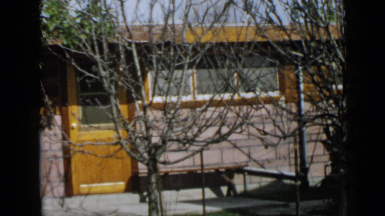 1949 San Diego residential exterior with an orange door, window band, porch railing, and leafless branches crossing the view.