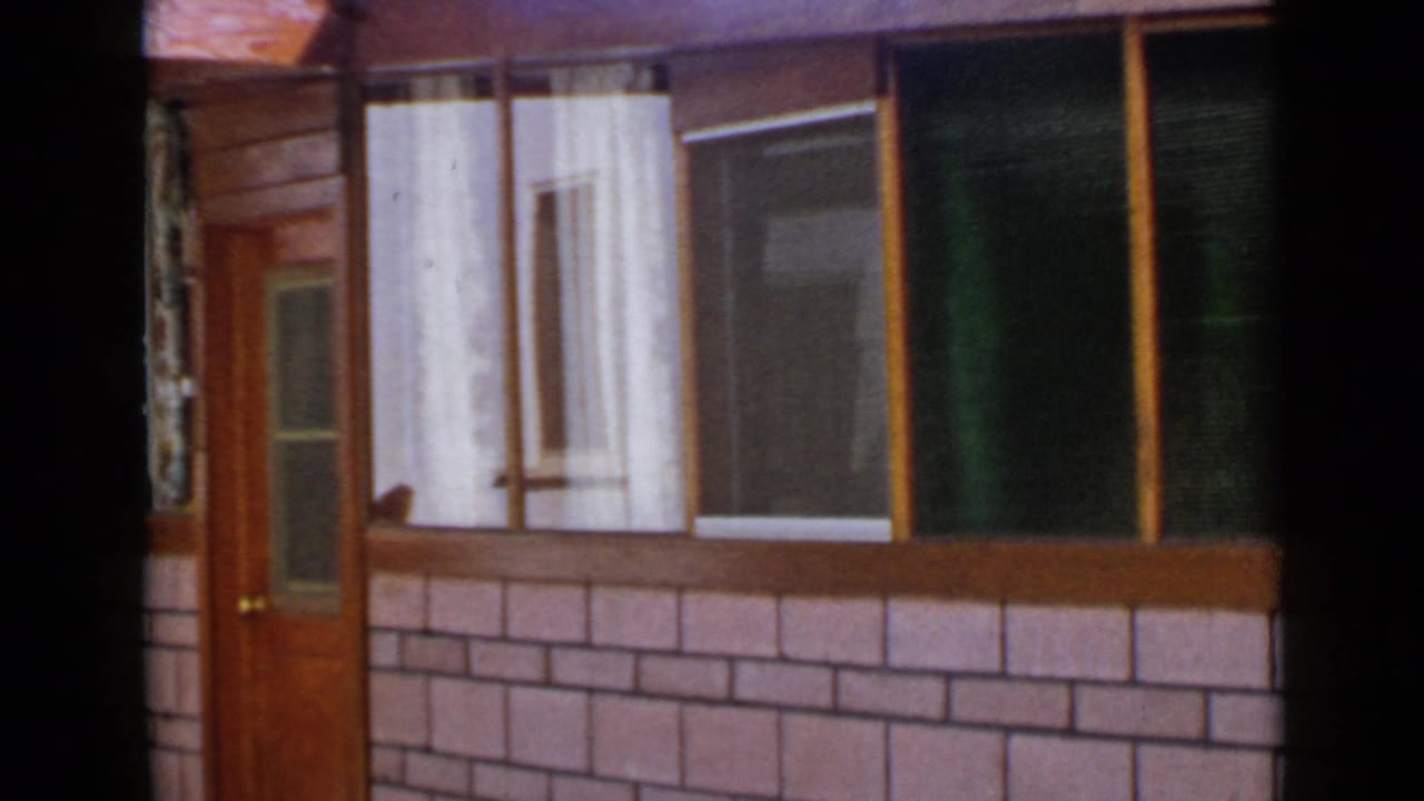 House facade with door, windows, curtains, and brick-pattern lower wall.
