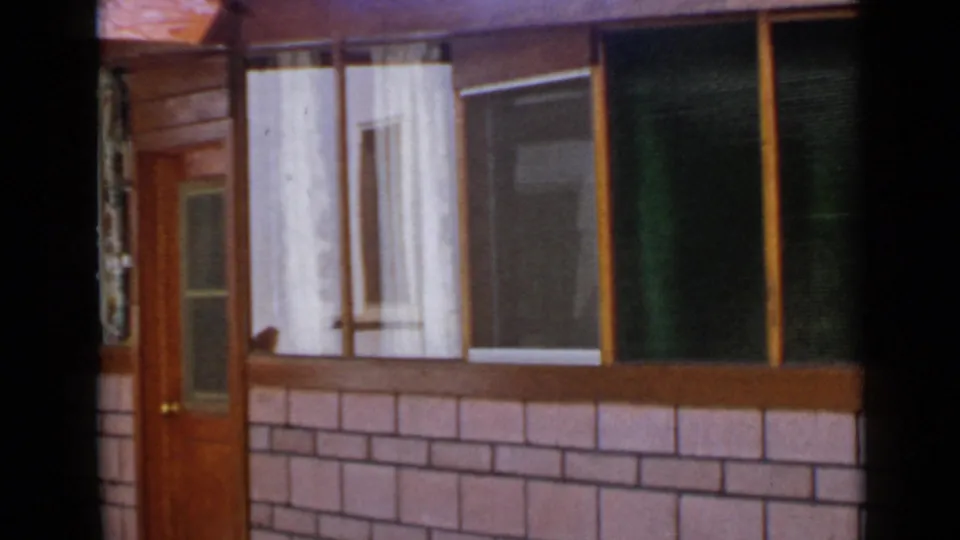 1949 San Diego exterior view of a modest residence with a wood-framed door, large windows, sheer curtains, and brick-pattern wall.