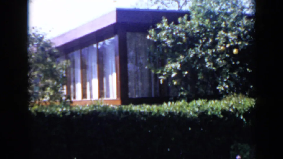 1949 San Diego frame showing a low residential structure with broad windows, a manicured hedge and surrounding trees.