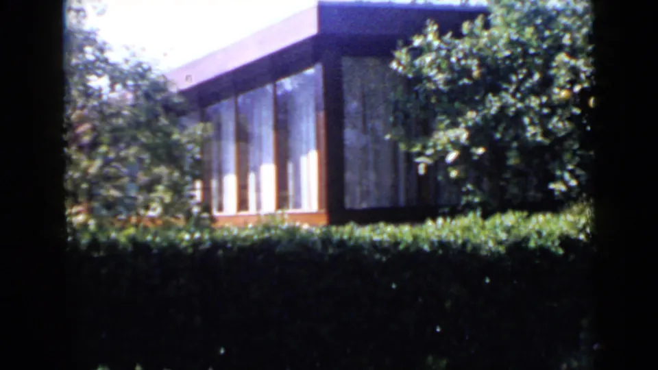 1949 San Diego home-movie frame with a closer view of the windowed exterior, hedge, roofline, and dense foliage.