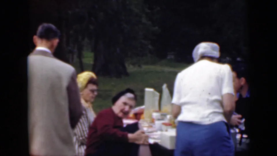 1949 San Diego outdoor picnic scene with adults in period clothing seated and standing around a white table set with food.