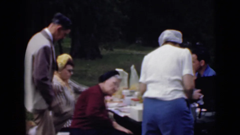 1949 San Diego home-movie frame of a man in a light suit and several adults around a picnic table in a park.