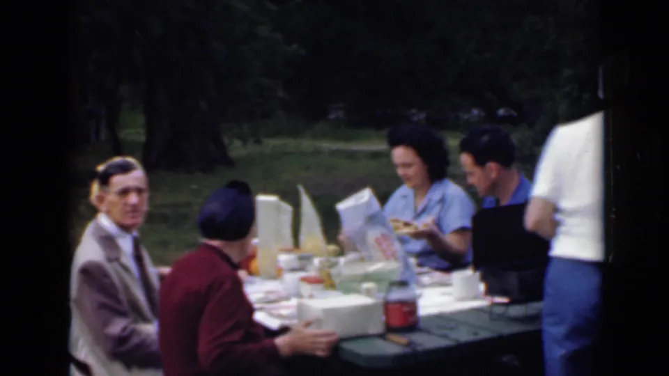 1949 San Diego picnic scene with adults seated at a table, food and drinks laid out, and one person cropped at the right edge.