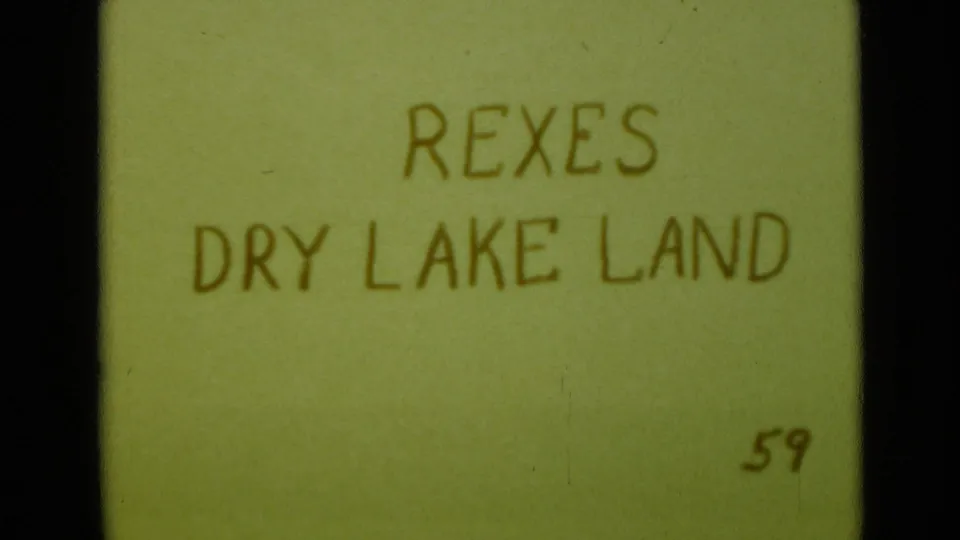 Handwritten home-movie title card reads REXES DRY LAKE LAND 59, shown on a green card with film grain and edge darkness.