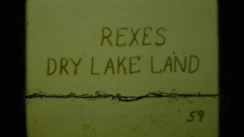 Handwritten 8mm title card reading REXES DRY LAKE LAND, with a horizontal scratch across the frame.