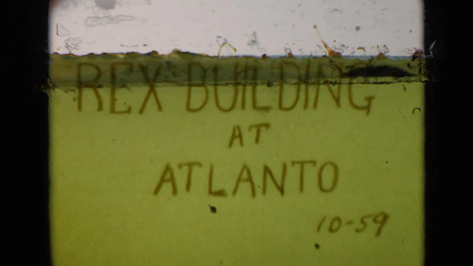 8mm frame of a handwritten green title card reading Rex Building at Atlanto, with a small 10-59 date and visible film wear.