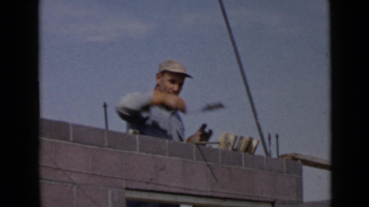 1949 San Diego construction footage frame with a laborer holding a trowel over a grey masonry wall.