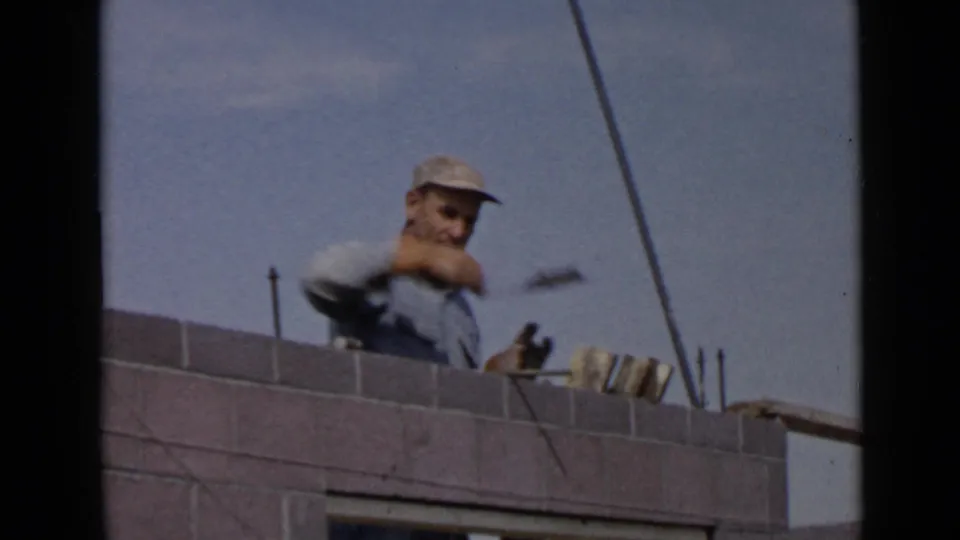 1949 San Diego construction footage frame with a laborer holding a trowel over a grey masonry wall.
