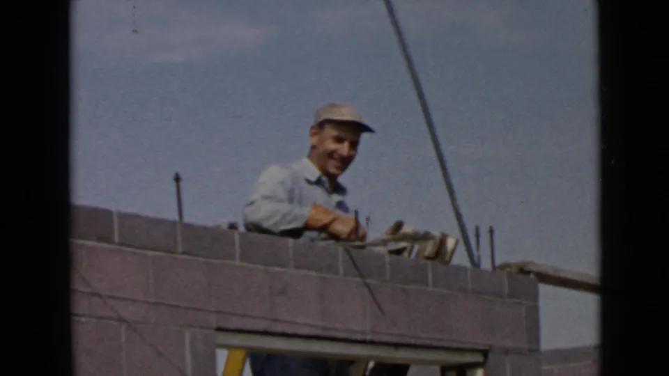 1949 San Diego frame showing a smiling construction worker behind a grey wall with an open doorway below.