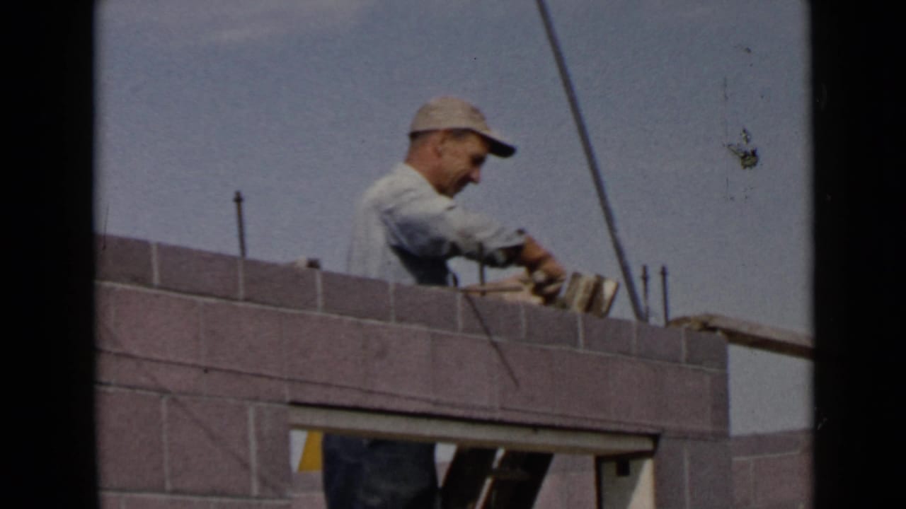Mason places or adjusts material along the top of a concrete block wall.