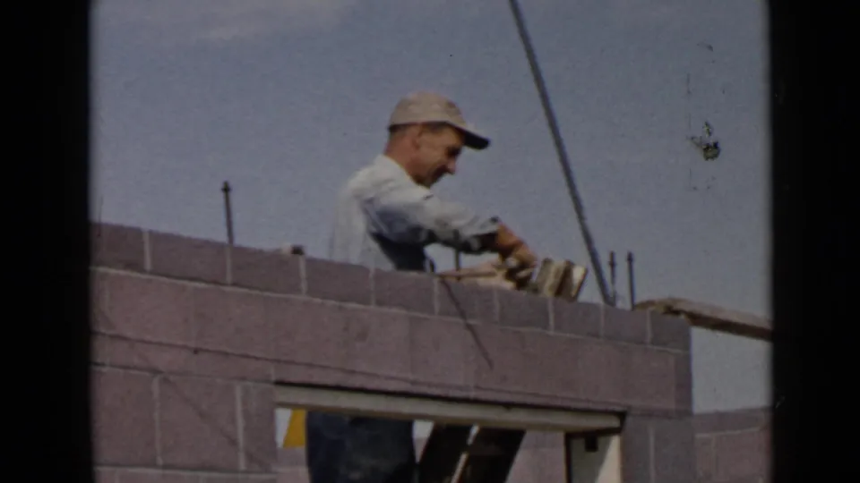 1949 San Diego 8mm frame showing a capped mason using his hands and tools along the top course of a concrete block wall.