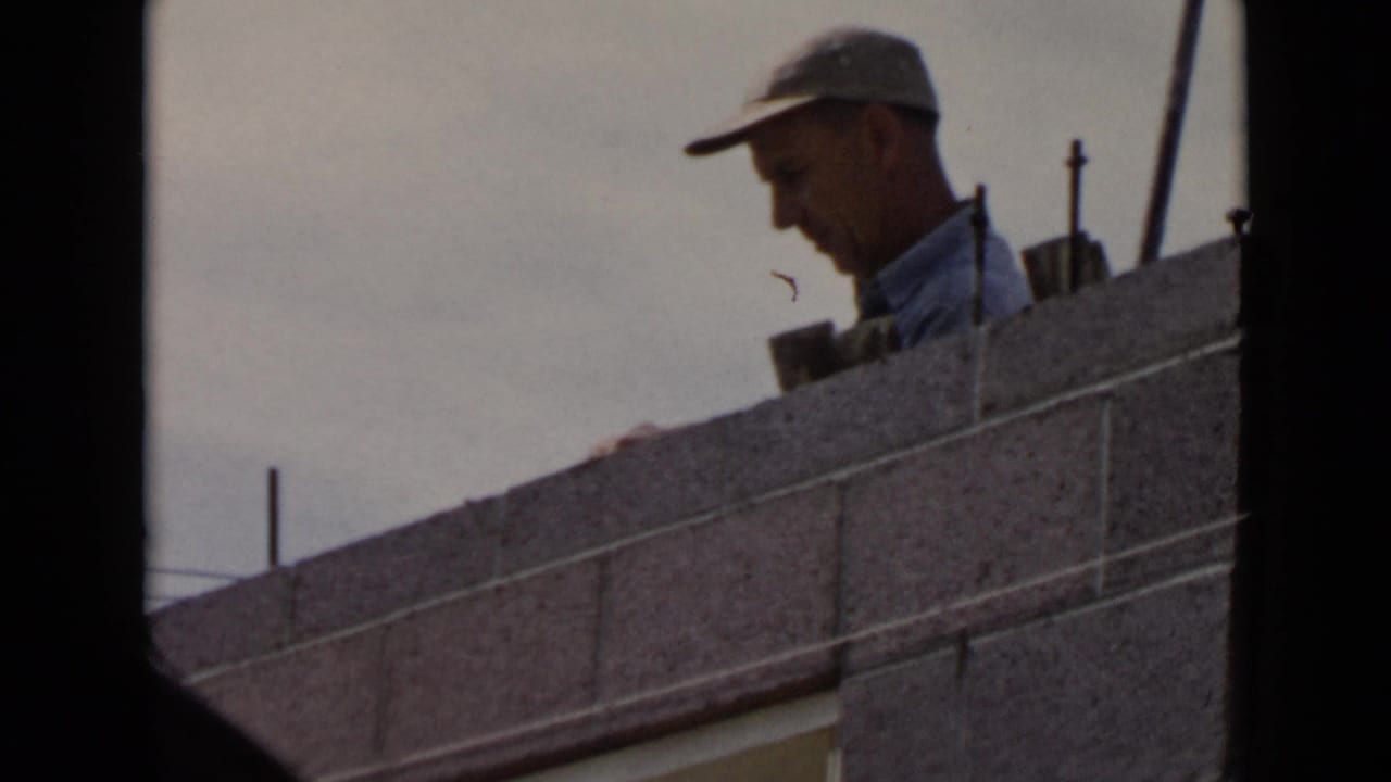 1949 San Diego home-movie frame showing a man in a light cap behind a partly built concrete block wall.