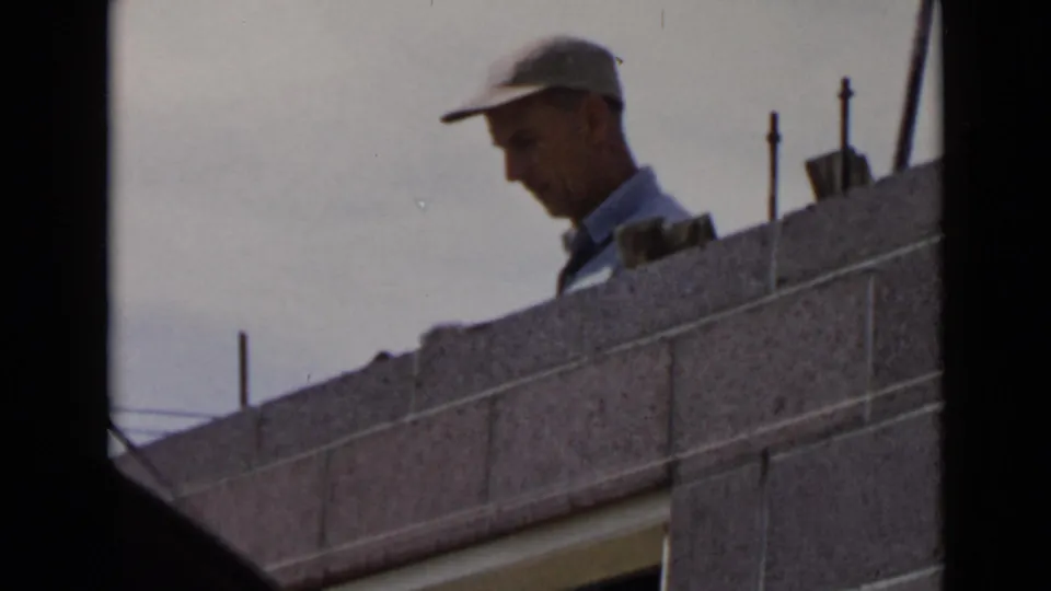 1949 San Diego home-movie frame with the worker partly silhouetted above a concrete block wall.