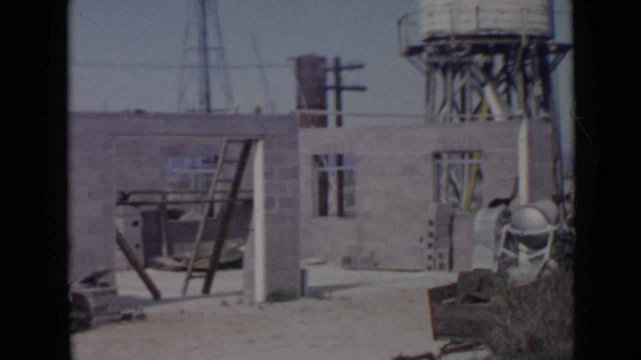 1949 San Diego construction site with unfinished cinder block walls, a leaning ladder, wheelbarrow, poles, and water tower.