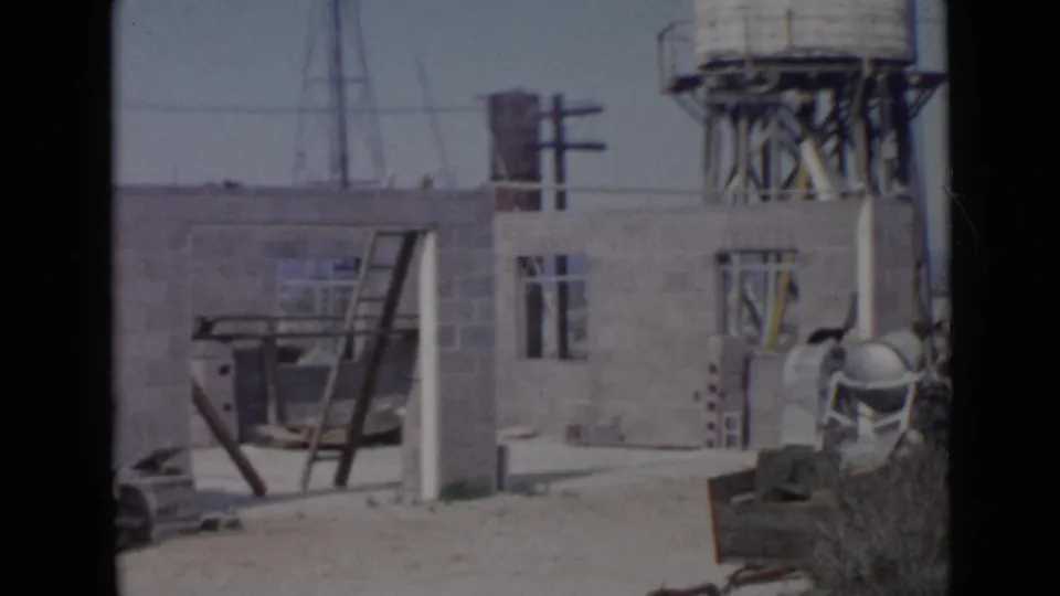 1949 San Diego construction site with unfinished cinder block walls, a leaning ladder, wheelbarrow, poles, and water tower.