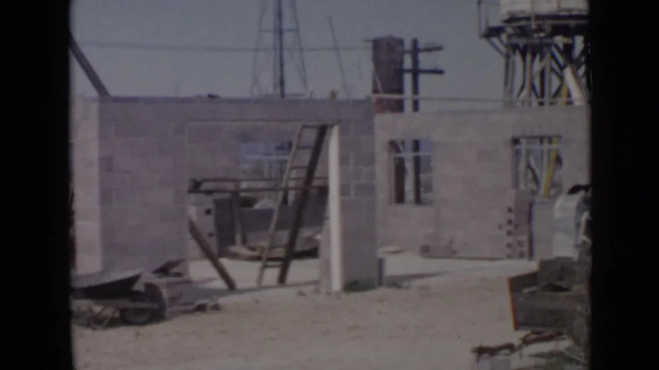 A 1949 San Diego work site shows block walls, window openings, a ladder, a wheelbarrow, utility poles, and a water tower.