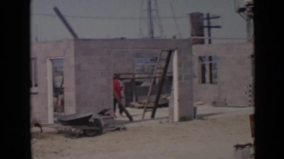 At the San Diego construction site, a worker in red stands by a leaning ladder beside unfinished cinder block walls.