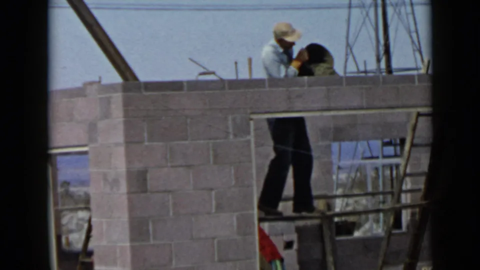 1949 San Diego home-movie frame showing a construction worker on a ladder beside a cinder block wall with exposed framing behind him.