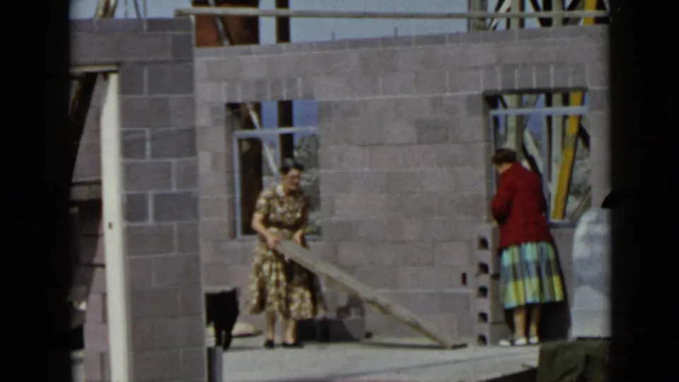 In the final frame, a woman lifts a long board near unfinished cinder block walls while a small black dog passes through.