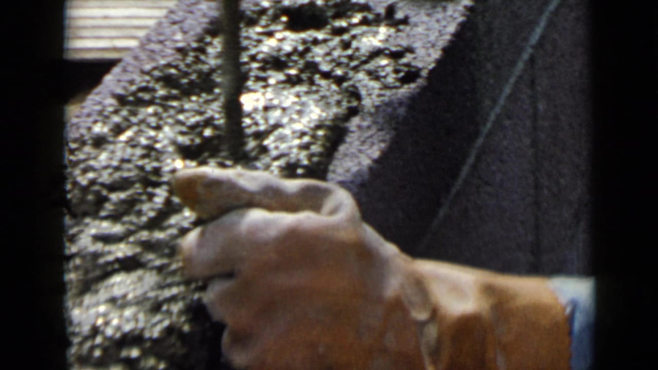 Close-up of a hand holding a trowel beside wet cement on a concrete block.