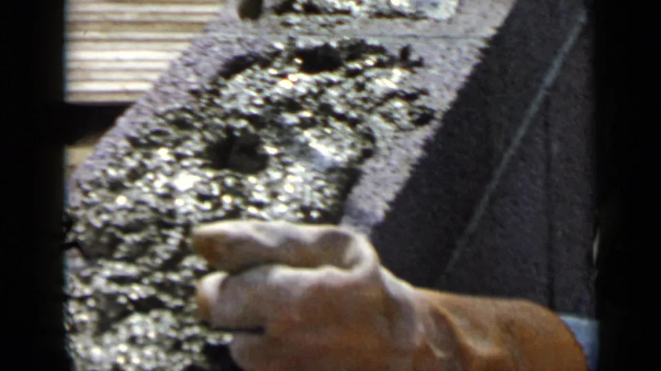 Close 8mm view of a worker's hand applying or smoothing cement on a concrete block in the San Diego construction footage.