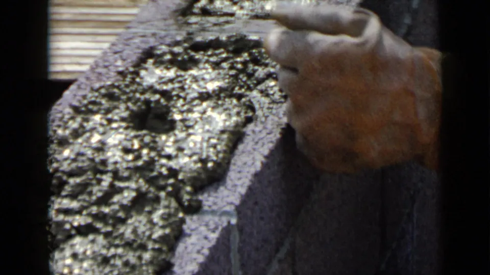 Close-up 8mm frame showing a worker's hand at the side of a cemented concrete block during construction work in San Diego.