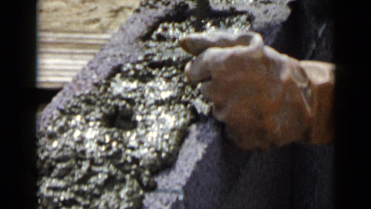 Close-up of a hand applying wet cement to a cinder block with a tool.